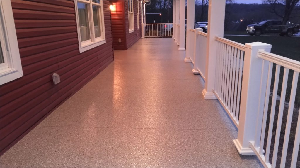 Long covered porch walkway with coated tan floor, white railing and red siding